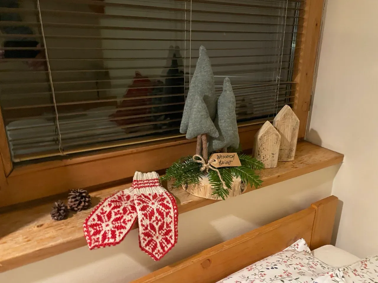 Christmas decorations on a wooden windowsill: felt trees, little wooden houses, pine cones and knitted mittens