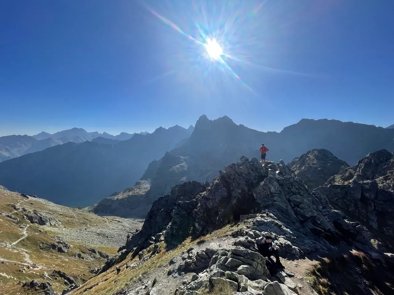 Granite peaks of the High Tatras in bright sunshine, seen from a trail, with a hiker on the rocks
